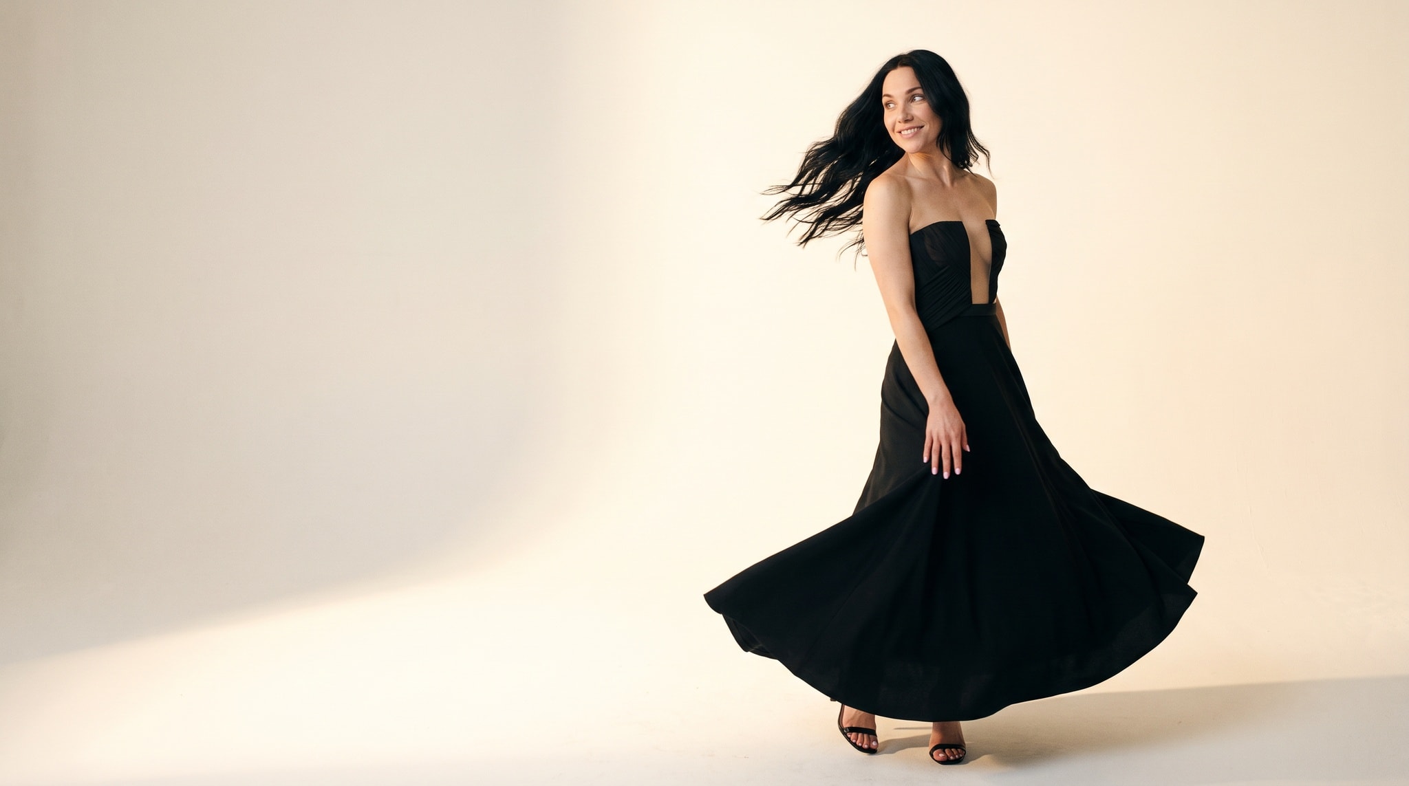 Anna in a black gown on a warm, high-key studio set, composed for a website header.