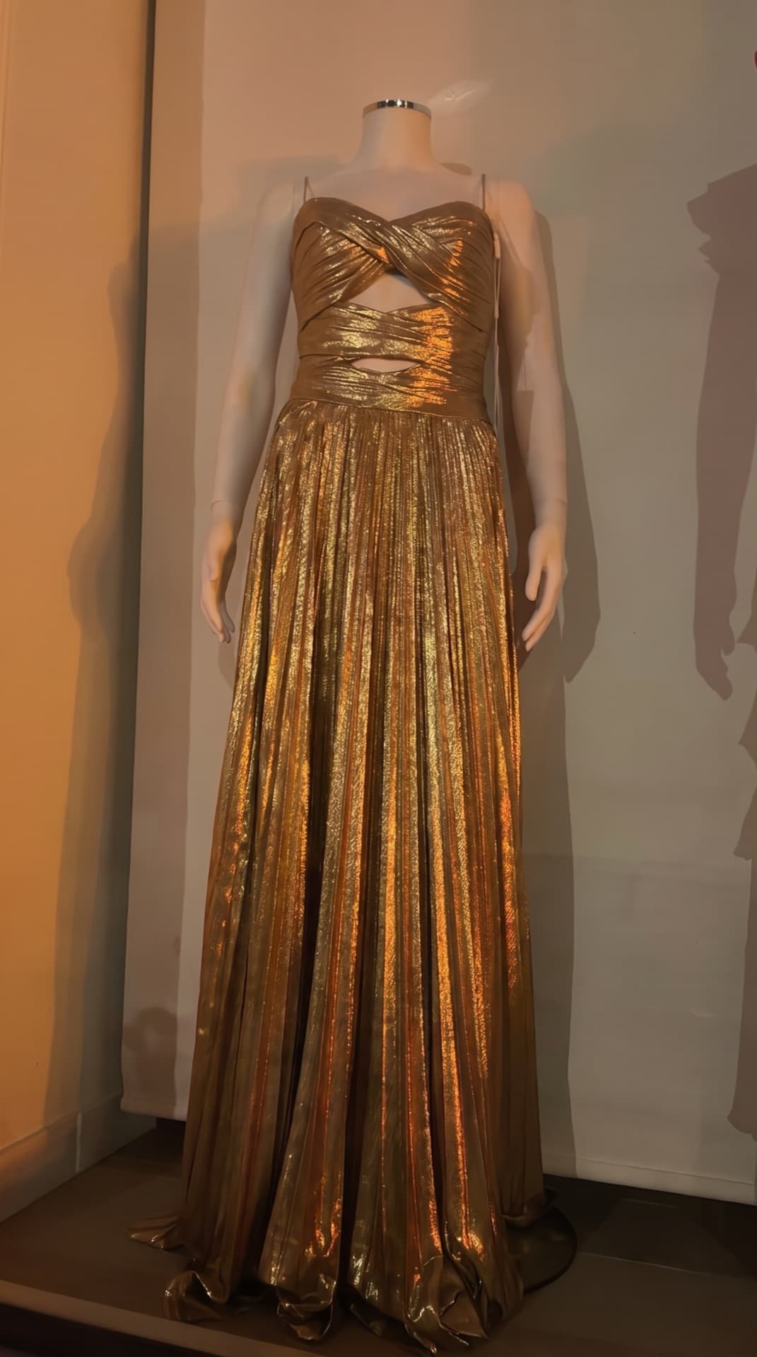 The boutique's own photo before Shoppermo: the gold gown on a mannequin in the shop window, under the shop's warm lighting.